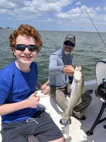 A joyful moment on the water as a young boy gives a thumbs up while holding a fish caught during a fishing trip, showcasing the excitement of a successful day on the boat.
