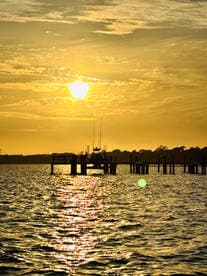 A serene sunset view featuring a boat docked at a pier, with golden reflections shimmering on the water — a picturesque scene perfect for evening cruises.