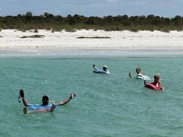 A group of friends enjoys a relaxing day floating in the clear waters near a sandy beach, perfect for summer fun and beach outings.