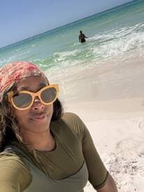 A woman enjoys a sunny day at the beach, capturing a selfie with the ocean waves in the background — a perfect moment for beach lovers.