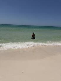 A person wades into the clear turquoise waters of a serene beach, perfect for relaxation and enjoying the sun.