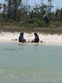 Two friends enjoy a relaxing moment on the beach, perfect for a sandbar stop or beach day with friends.