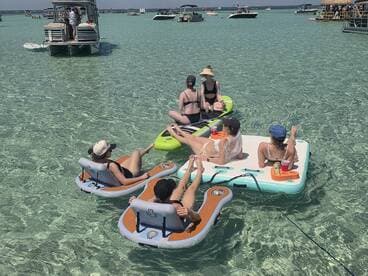 A lively group enjoys a day on floating mats in crystal-clear waters, sipping cocktails and soaking up the sun — the perfect summer getaway.