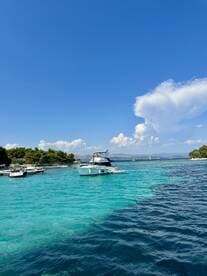 A scenic view of a boat cruising through stunning turquoise waters, surrounded by lush greenery and a clear blue sky — perfect for summer adventures on the water.