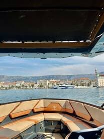 A stylish interior view of a boat's seating area, showcasing comfortable cushions and a scenic backdrop of the waterfront and mountains.