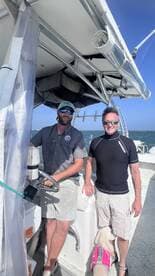 Two men enjoy a day on the water aboard a boat, with one at the helm and a dog by their side — perfect for a fun day out on the sea.