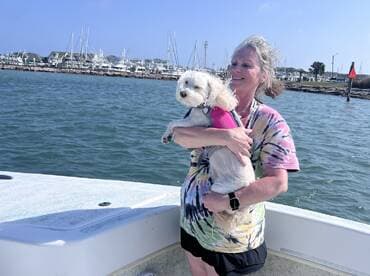 A joyful moment on the water as a woman holds her dog while enjoying a boat ride, showcasing the fun of bringing pets along for aquatic adventures.