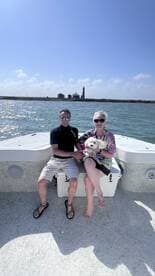 A couple enjoys a sunny day on their boat with their dog, capturing a perfect moment against the backdrop of a lighthouse.