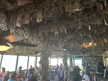 Inside a lively boat-themed restaurant adorned with dollar bills, patrons enjoy their meals in a unique and vibrant atmosphere.
