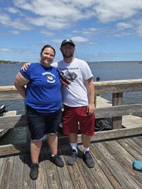 A cheerful couple poses for a photo on the dock, with a scenic waterfront view in the background — perfect for capturing memories of a day by the water.