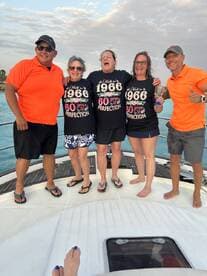 A joyful group celebrates a milestone birthday aboard a boat, showcasing camaraderie and fun in a beautiful setting.