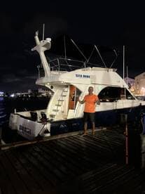 A man poses in front of the luxurious 'Sea Blue' yacht at night, showcasing the vibrant atmosphere of a dockside celebration.
