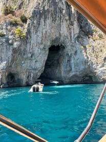 A boat approaches a stunning cave entrance surrounded by cliffs, showcasing the vibrant turquoise waters — a perfect scene for adventure seekers exploring coastal wonders.