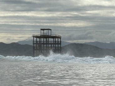 An unclear image featuring a structure by the water, with waves crashing in the foreground. The scene lacks identifiable subjects or clarity.
