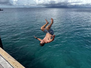 A man performs an impressive flip into the clear turquoise waters, capturing the thrill of summer fun and water activities.