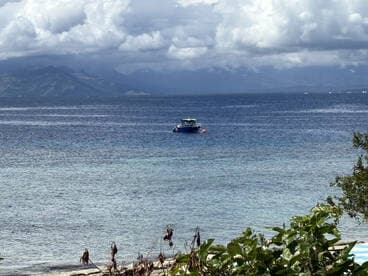 A serene view of a boat anchored in calm waters, surrounded by lush greenery and distant mountains, perfect for showcasing tranquil marine settings.