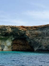 A stunning view of a rocky coastline featuring a natural cave, showcasing the beauty of the surrounding turquoise waters — perfect for eco tours and scenic boat trips.