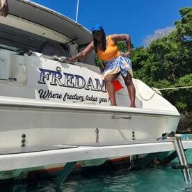A woman poses on the side of the boat named 'FREDAM' under a clear blue sky, showcasing a vibrant day on the water — perfect for memorable boating adventures.