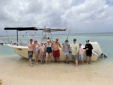 A cheerful group of friends and family poses on the beach next to their boat, enjoying a fun day in the sun — perfect for memorable beach outings.