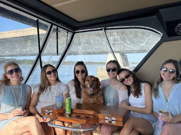 A joyful group of friends relaxes inside a boat, enjoying drinks and the company of a golden retriever — perfect for memorable outings on the water.