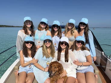 A cheerful group of friends poses on a boat, enjoying a sunny day on the water with their golden retriever — perfect for memorable outings and celebrations.