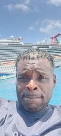 A man poses for a selfie with a cruise ship in the background, capturing a moment of fun in the sun while enjoying a day on the water.