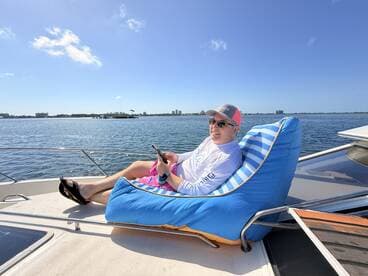 A man relaxes on a colorful bean bag chair aboard a boat, enjoying the sunny weather and beautiful water views — a perfect moment for leisure on the water.