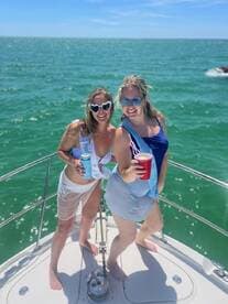 Two friends celebrate on the bow of a boat, enjoying drinks and sunshine — perfect for bachelorette parties or fun days on the water.