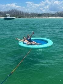 Two friends enjoy a sunny day on a floating mat in clear waters, sipping cocktails and soaking up the sun — a perfect way to relax during a boating adventure.