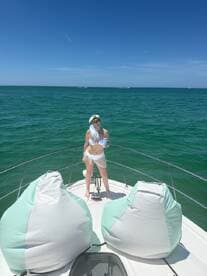 A young woman enjoys a refreshing drink while relaxing on the bow of a boat under the bright sun, showcasing a perfect day on the water.
