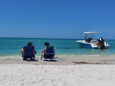 A couple relaxes on the beach while a boat is anchored nearby, creating a perfect scene for a day of sun and fun on the water.