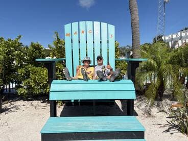 A cheerful couple enjoys a sunny day at Mango's, posing on a giant beach chair — a perfect spot for memorable vacation photos.