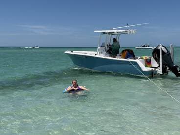 A woman enjoys a relaxing swim near a boat in clear turquoise waters, capturing the essence of a perfect beach day filled with fun and water activities.