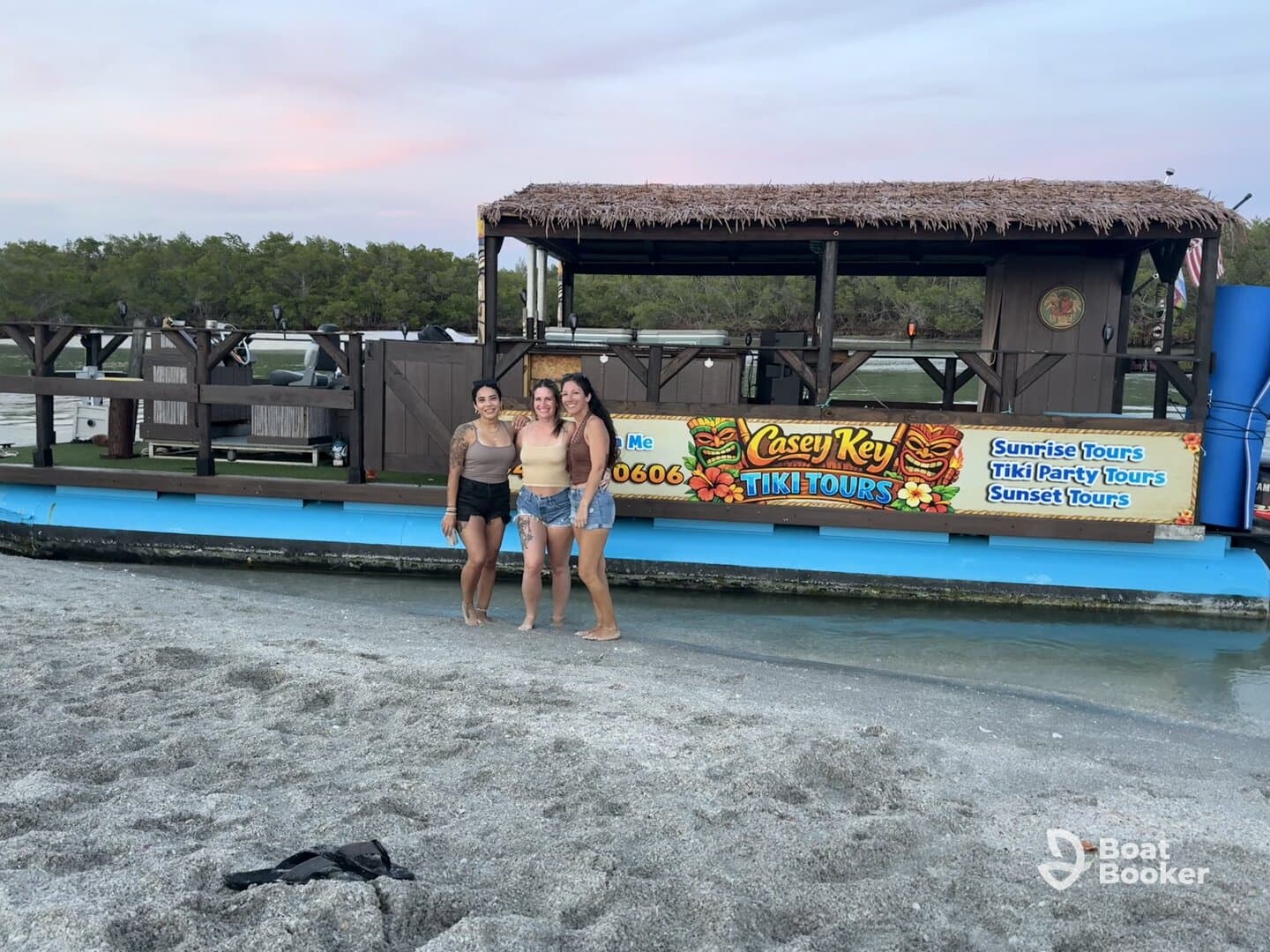 Three friends pose in front of the vibrant Casey Key Tiki Tours boat, ready for a fun-filled adventure on the water — perfect for sunset tours and party experiences.