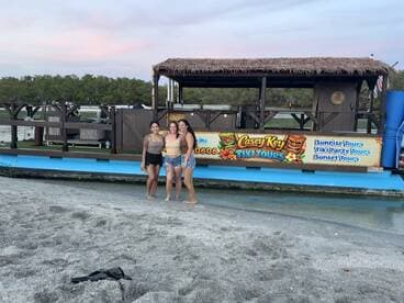 Three friends pose in front of the vibrant Casey Key Tiki Tours boat, ready for a fun-filled adventure on the water — perfect for sunset tours and party experiences.