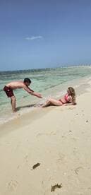 A couple enjoys a playful moment on the beach, with the clear waters and sandy shore creating a perfect backdrop for a romantic getaway.