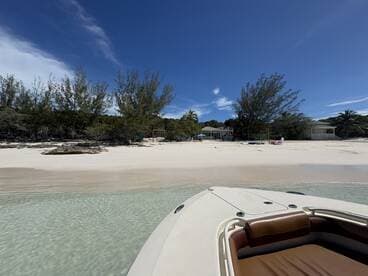 A serene view of a beach with clear waters and lush greenery, featuring the bow of a boat in the foreground — an ideal spot for relaxation and exploration.