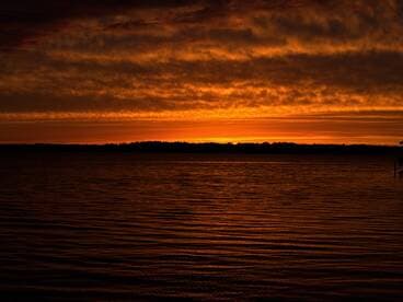 A stunning sunset casts vibrant orange hues over the water, creating a serene backdrop perfect for evening boat outings.