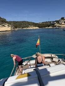 Two guests enjoy the beautiful coastline from the deck of a boat, with clear turquoise waters inviting them for a swim — a perfect day on the water.