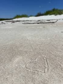 A close-up shot of a sandy beach with a heart drawn in the sand, but the image is unclear and lacks distinct features.