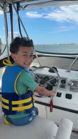 A young boy joyfully steers a boat while wearing a life jacket, capturing the excitement of a fun day on the water.