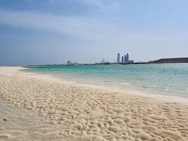 A stunning view of a sandy beach with turquoise waters and a skyline in the background, perfect for showcasing beautiful coastal destinations.