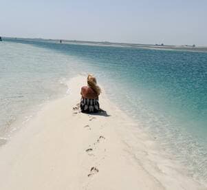 A woman enjoys a moment of solitude on a sandy beach, with footprints leading into the tranquil waters — a perfect escape for relaxation and reflection.