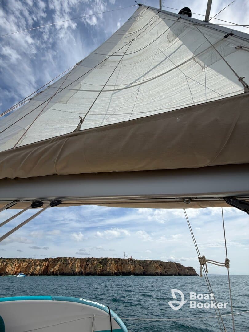 A stunning view of a sailboat's sail against a backdrop of rocky cliffs, showcasing the beauty of sailing on open waters.