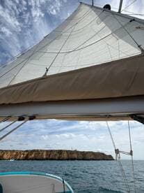A stunning view of a sailboat's sail against a backdrop of rocky cliffs, showcasing the beauty of sailing on open waters.