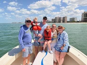 A joyful family enjoys a sunny day on the water, posing together on their boat with life jackets, surrounded by a beautiful waterfront backdrop.