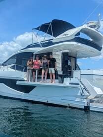 A cheerful group poses on the deck of a luxurious yacht, celebrating their time on the water under a clear blue sky.
