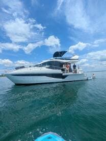 A lively group enjoys a sunny day on the water, with some swimming near a stylish yacht — perfect for summer adventures and fun on the lake.