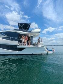 A lively group enjoys a sunny day on a yacht, with some swimming nearby and others relaxing on deck — the perfect setting for a summer party on the water.