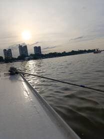 A serene view of a boat's edge with the sun setting in the background, showcasing the tranquil waters and urban skyline.